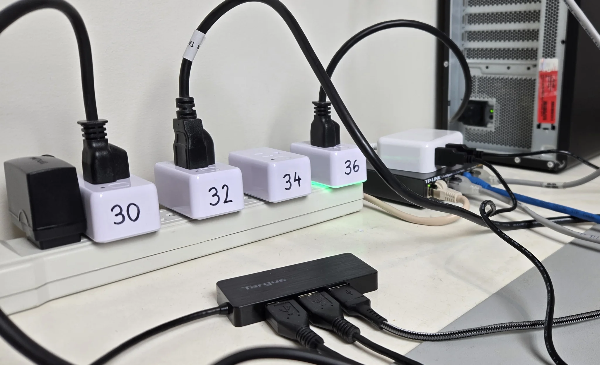 The automated test bench: a power bar with four Shelly smart plugs, each labeled with the last number of its IP address (30, 32, 34 and 36) and each powering one dev board; a USB hub for the boards’ USB-UART and JTAG connections; a TP-Link Gigabit Ethernet switch that connects the boards to the network; and, in the top right, a host PC with an NVIDIA GPU and a ConnectX-6 NIC.